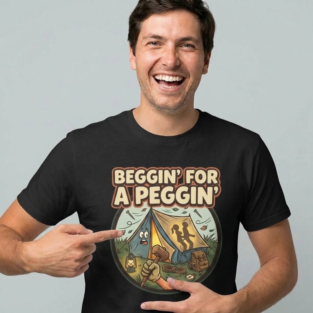 A smiling man points to his Beggin' for a Peggin' Camping Tee, featuring the slogan above a cartoon campsite with two shadowy figures in a tent—ideal as a festival outfit or cheeky camping gift.