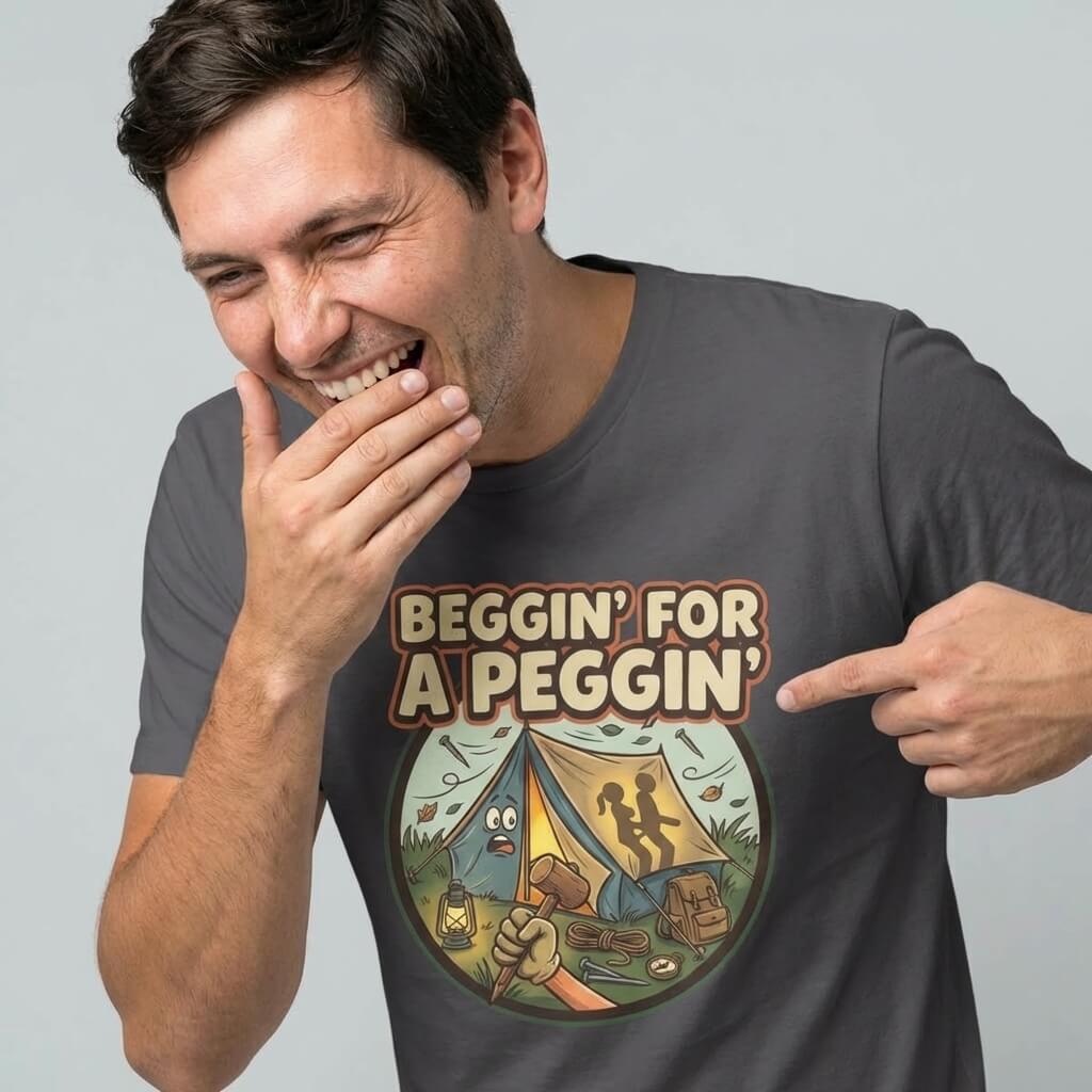 A man laughs while pointing at his Beggin' for a Peggin' Camping Tee, featuring a cartoon tent with silhouettes and the text "BEGGIN FOR A PEGGIN"—a funny, rude camping shirt perfect as a quirky gift or festival outfit.