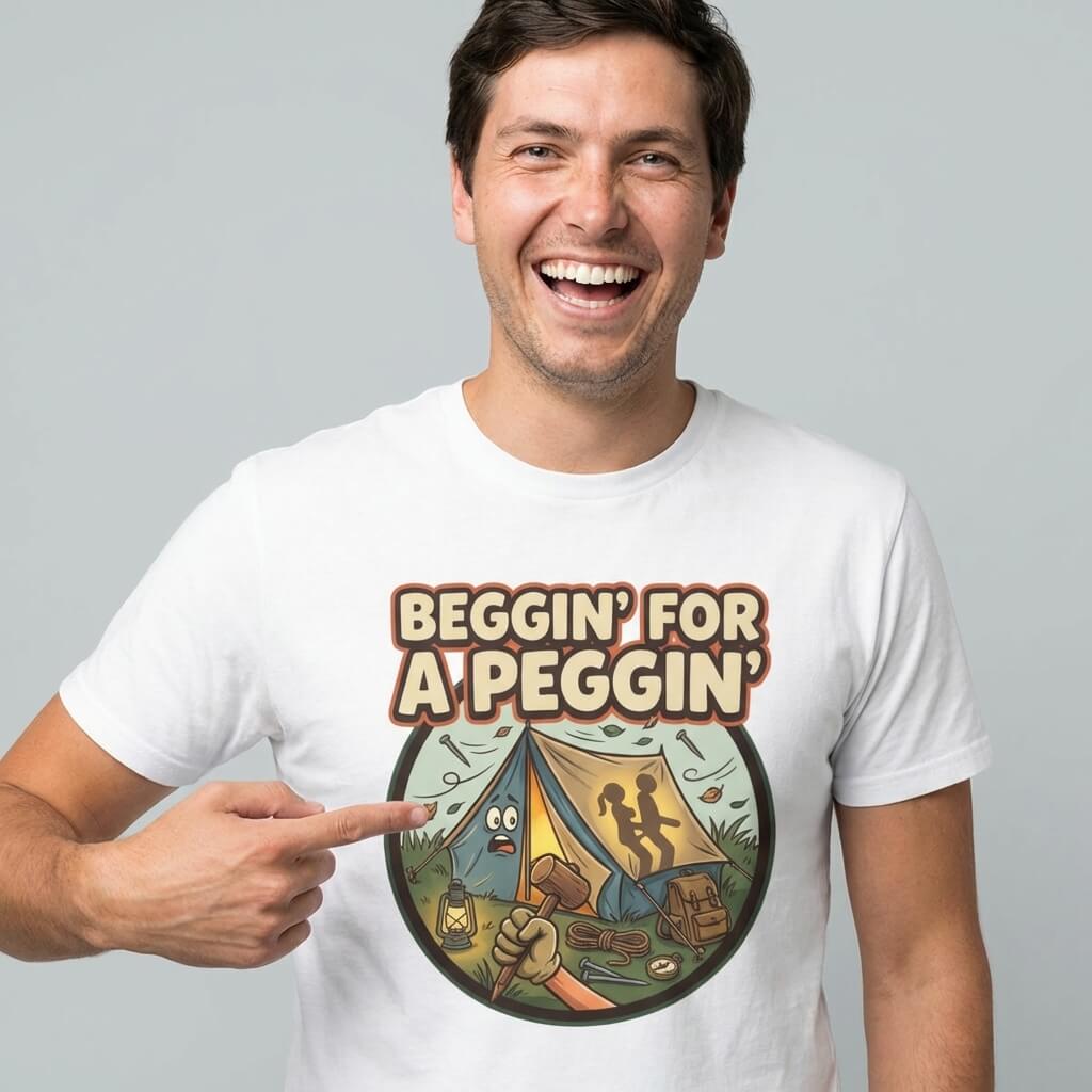 A smiling man points at his "Beggin' for a Peggin' Camping Tee," which features a cartoon tent, camping gear, and two silhouetted figures—perfect for festival outfits or as a cheeky gift for friends.