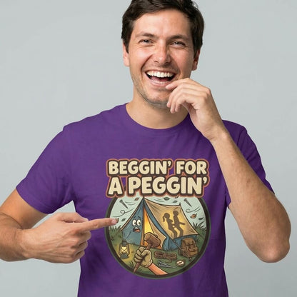 A smiling man wears the Beggin' for a Peggin' Camping Tee, a purple shirt with a cartoon camp scene and two silhouettes in a tent—an ideal rude gift or quirky festival outfit.