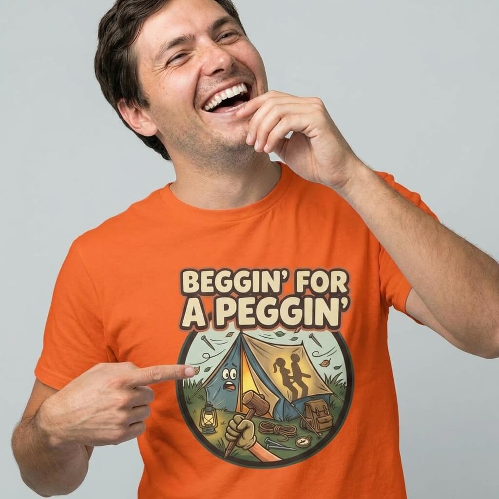 A smiling person in an orange shirt points to their Beggin’ for a Peggin’ Camping Tee, a funny t-shirt with a cartoon campsite and bold text—perfect as a rude gift or for festival outfits.
