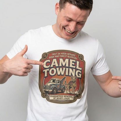 A smiling man points at his Camel Towing Funny Tee, a white graphic t-shirt with a vintage tow truck and camel logo, plus the phrases "Fast 24 Hour Service" and "Guaranteed Removal of Heavy Loads"—a great novelty gift.