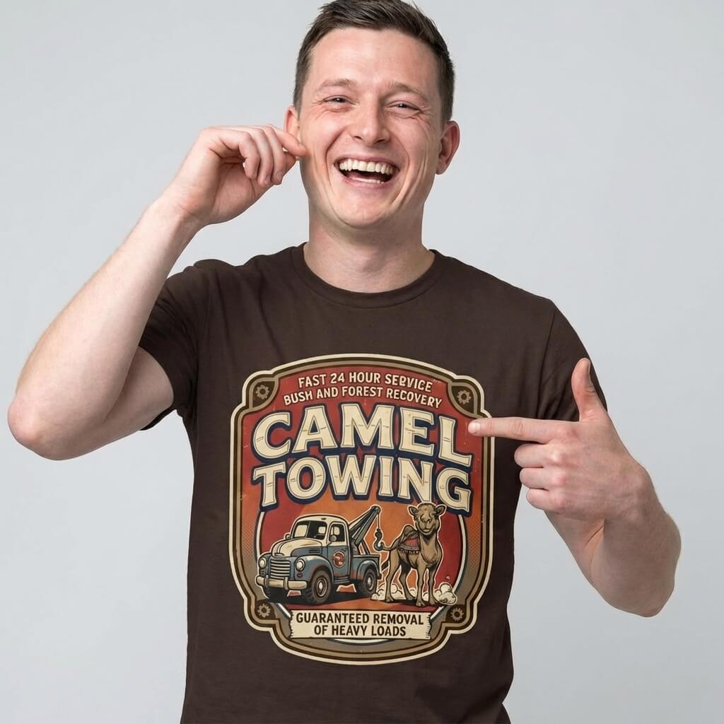 A smiling man points to his Camel Towing Funny Tee, a novelty graphic shirt with a vintage tow truck, camel illustration, and “Camel Towing: Guaranteed Removal of Heavy Loads”—the perfect funny gift.