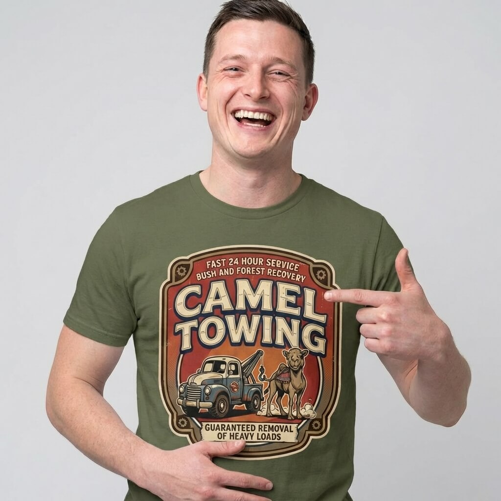 Wearing the Camel Towing Funny Tee in olive green, a smiling man points to its tow truck and camel graphic with the slogan "Guaranteed removal of heavy loads”—a hilarious novelty gift for any occasion.