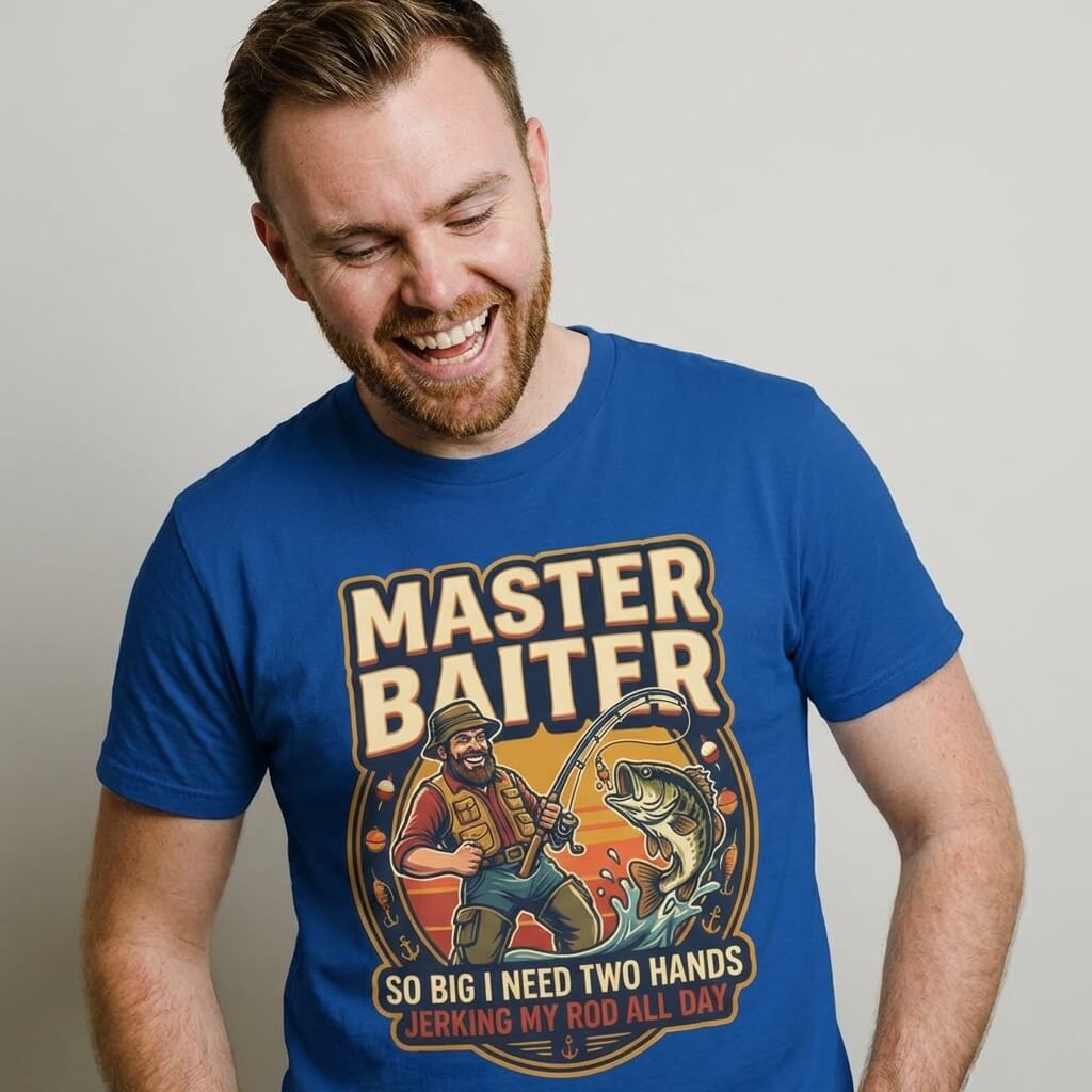 A smiling man wears the Master Baiter Rude Fishing Tee, a blue shirt with a cartoon fisherman reeling in a huge catch and the cheeky slogan: "So Big I Need Two Hands Jerking My Rod All Day," perfect for laughs on any fishing trip.