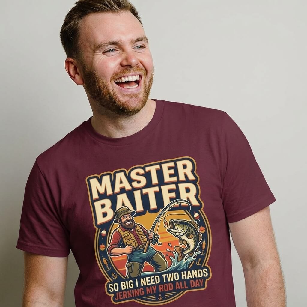 A smiling man with short hair and a beard wears the Master Baiter Rude Fishing Tee, a funny maroon shirt featuring a cartoon fisherman, a big fish, and the cheeky caption “SO BIG I NEED TWO HANDS JERKING MY ROD ALL DAY.”.