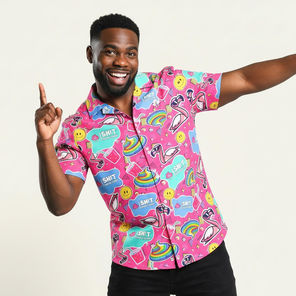 A smiling man strikes a playful pose in the Badass Shirt, a brightly colored top adorned with rainbows, smiley faces, and whimsical pink flamingos, set against a plain white background.