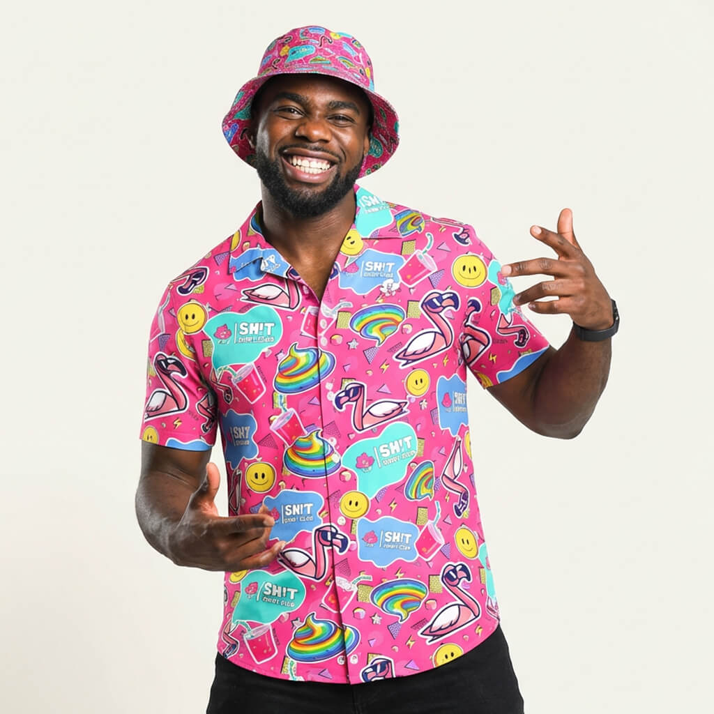 Wearing the Badass Shirt—a bright pink top with bold, playful patterns like rainbows and smiley faces—a smiling man in a colorful bucket hat gestures with both hands, radiating whimsical fun.