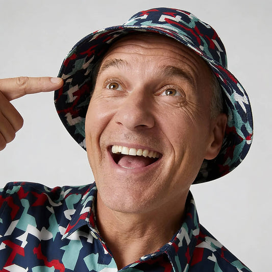 A joyful middle-aged man in a colorful shirt points at his Combat2Coffee Army Camo Bucket Hat, smiling and looking upward.
