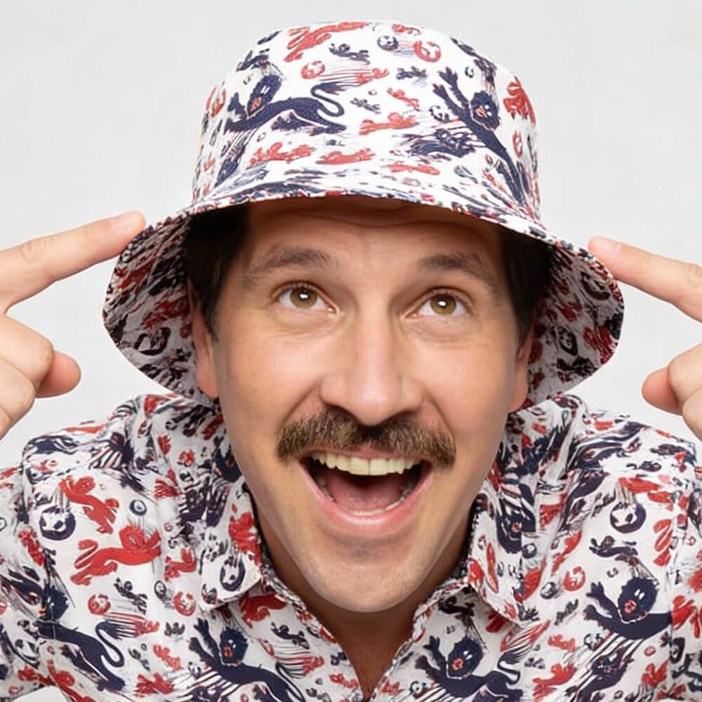 A smiling man with a mustache excitedly points at his England Football Bucket Hat, which features a red, white, and blue crab and sea creature pattern.
