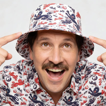 A smiling man with a mustache excitedly points at his England Football Bucket Hat, which features a red, white, and blue crab and sea creature pattern.