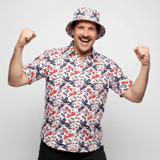 A smiling man with a mustache wears the England Football Hawaiian Shirt, raising both fists in excitement against a plain light gray background.