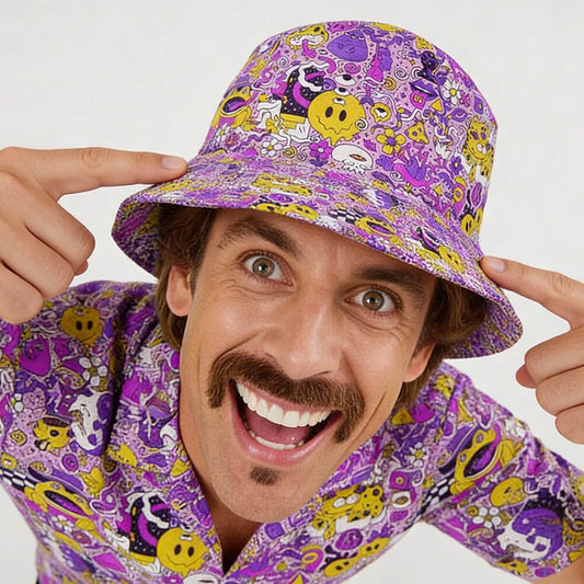 A smiling man with a mustache points at his Magical Psychedelic Bucket Hat, which matches his shirt. The hat features yellow smiley faces and whimsical patterns—perfect for festival fashion. The background is plain white.