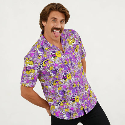 A playful man with brown hair and a mustache smiles and sticks out his tongue while wearing the Magical Psychedelic Shirt, a colorful fashion top with cartoon faces, smiley emojis, and vibrant designs on a white background.