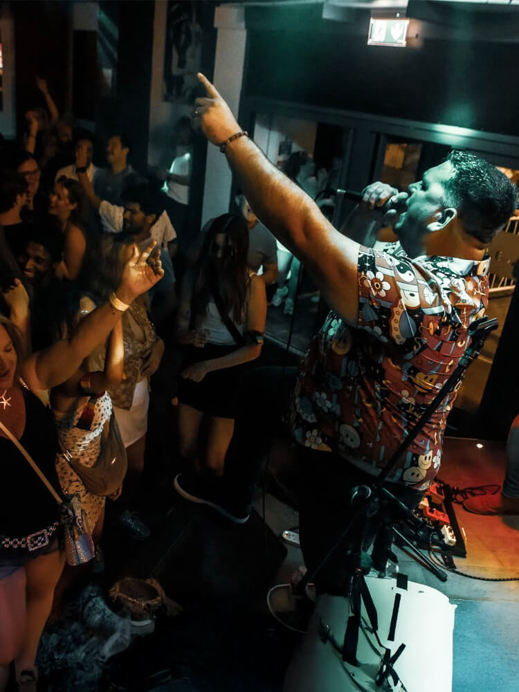 Person wearing a party shirt on stage with microphone pointing at audience in a dark indoor setting