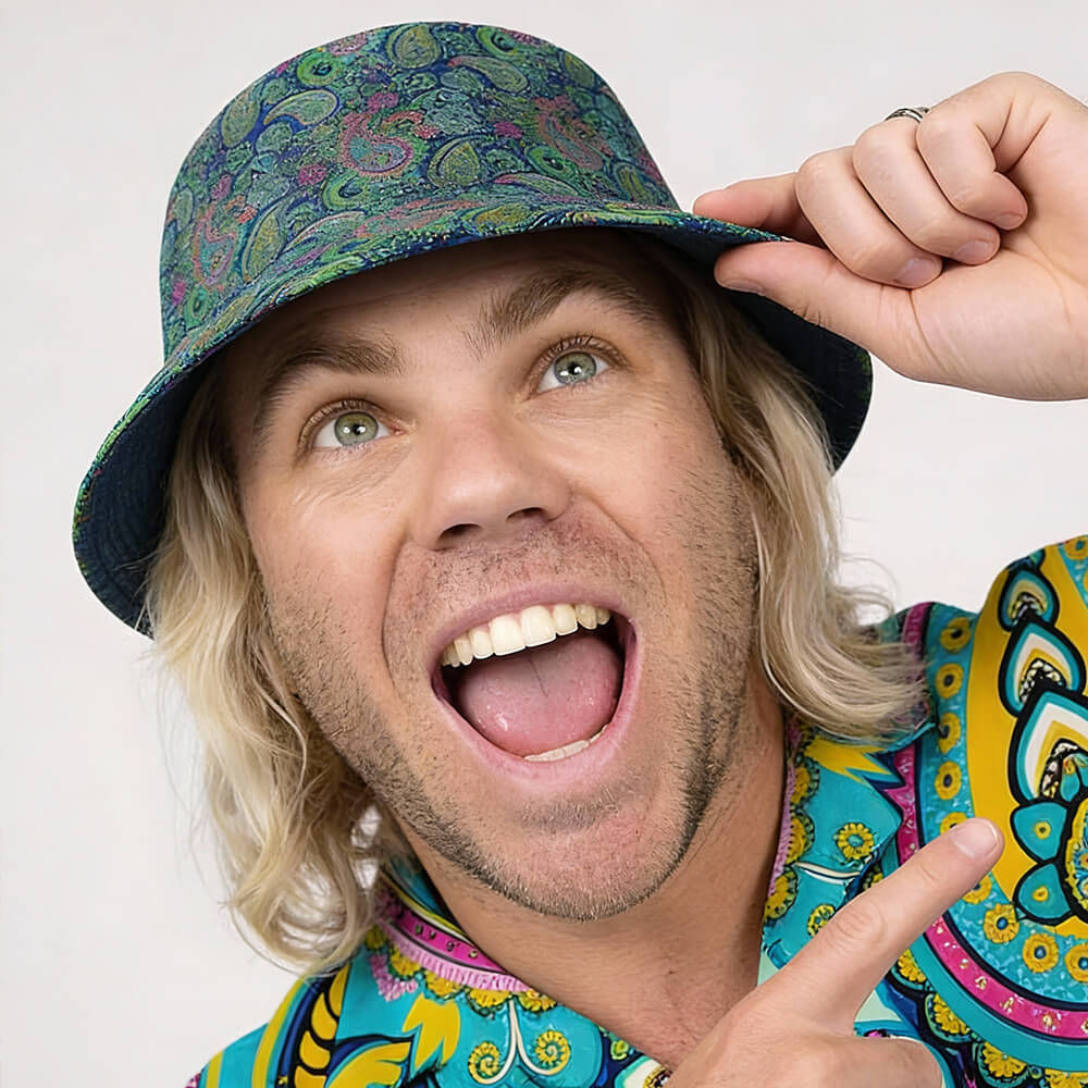 A smiling person with long blonde hair wears the Psychedelic Explorer Bucket Hat and a matching shirt, holding the hat with one hand and pointing upward with the other, looking cheerful and excited.