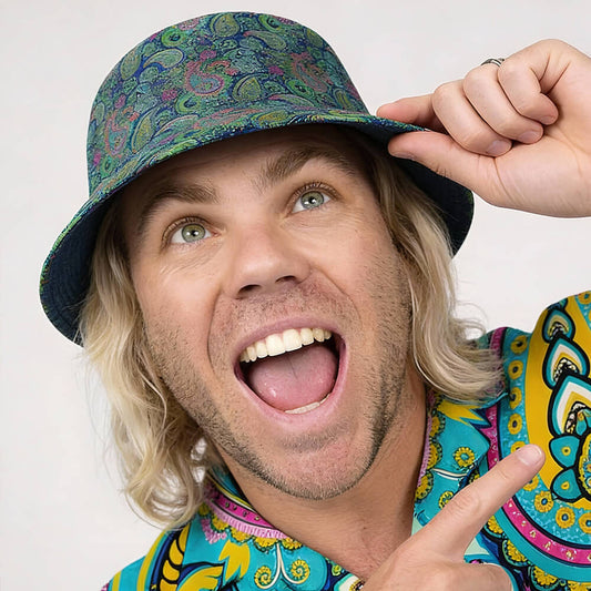 A smiling person with long blonde hair wears the Psychedelic Explorer Bucket Hat and a matching shirt, holding the hat with one hand and pointing upward with the other, looking cheerful and excited.