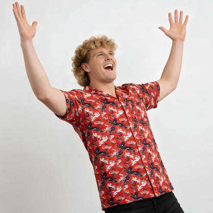 A joyful person with curly blonde hair raises their arms while wearing the Red England FC Hawaiian Shirt, standing against a plain white background.