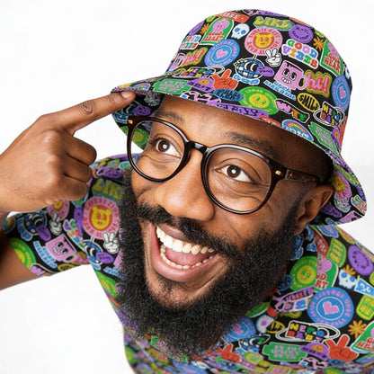 A smiling man in glasses and a patterned shirt points to his Retro Sticker Bucket Hat, featuring colorful 90s cartoon graphics, peace signs, and nostalgic phrases like WOW and LIKE on a white background.
