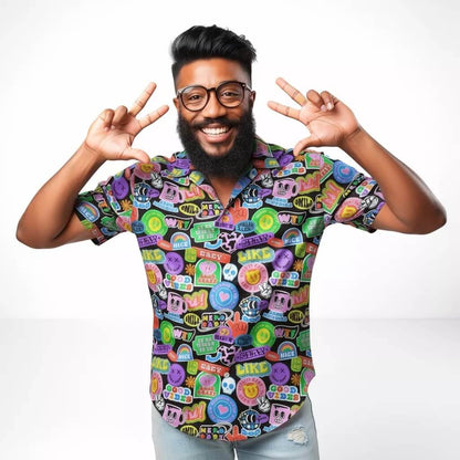 A bearded man with glasses smiles and flashes peace signs with both hands while wearing the Retro Sticker Shirt against a plain white background.