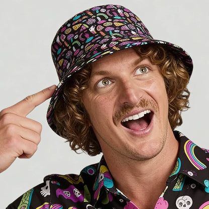 A smiling man with curly hair and a mustache points at his Shroom Bucket Hat, which features playful psychedelic patterns. He wears a matching vibrant shirt with fun, cartoon-style designs.