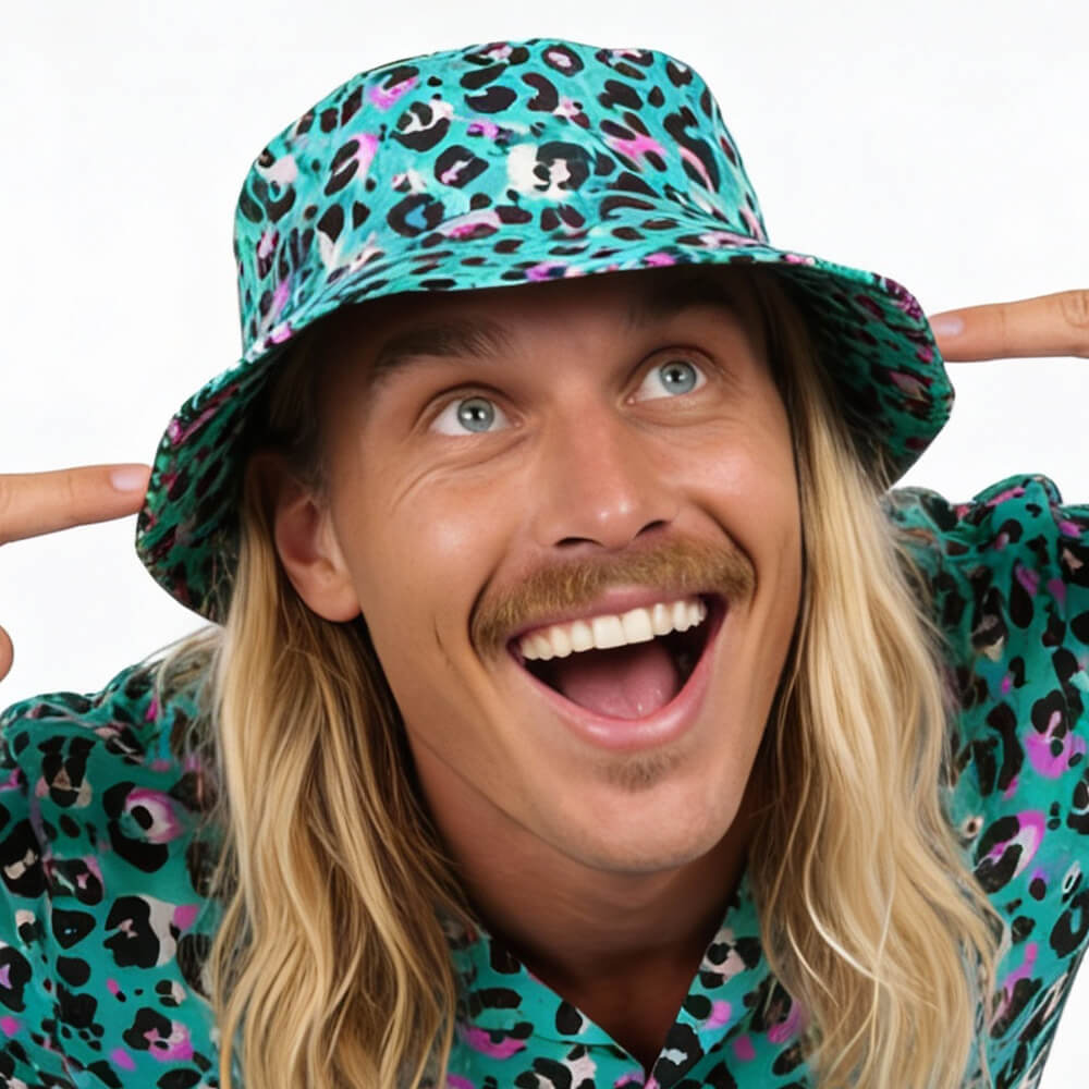 A smiling person with long blond hair and a mustache cheerfully points to their Turquoise Tempest Leopard Print Bucket Hat, matching it with their shirt, standing against a white background.