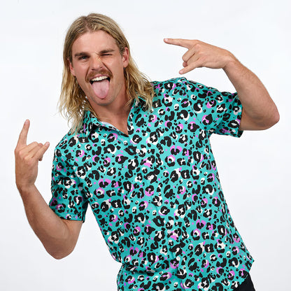 A man with long blond hair and a mustache winks, sticks out his tongue, throws rock hand gestures, and stands out in a Turquoise Tempest Leopard Print Shirt against a plain white background.