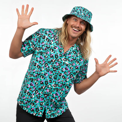 A smiling person with long blonde hair wears the Turquoise Tempest Leopard Print Shirt and matching bucket hat, raising both hands excitedly against a plain white background.