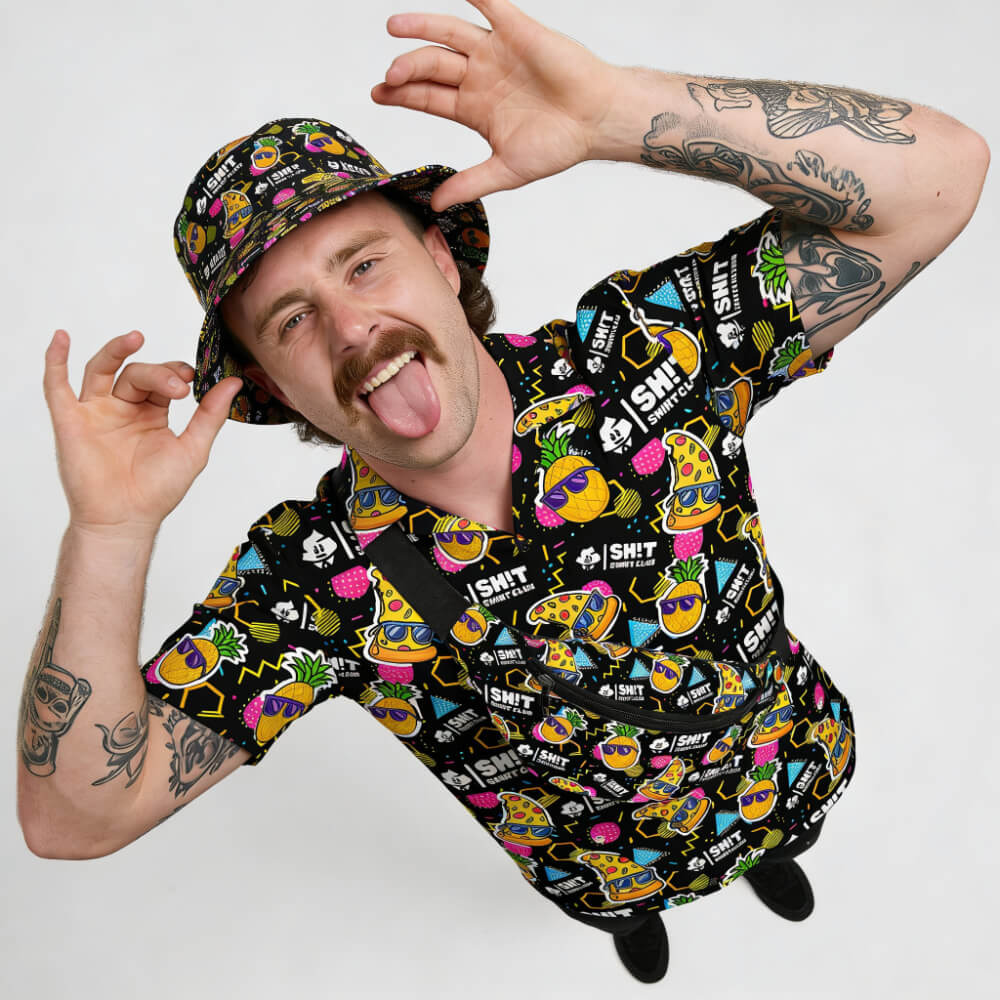 A man with tattoos and a mustache playfully sticks out his tongue while wearing the Wanna Pizza This Shirt and a matching bucket hat with cartoon food patterns, looking up at the camera against a plain background.