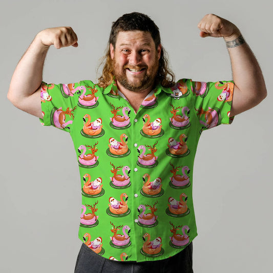 A smiling man with long hair and a beard flexes his arms, wearing the bright green "Sleigh My Name, Sleigh My Name Shirt" decorated with cartoon animals riding bumper cars. The background is plain gray.