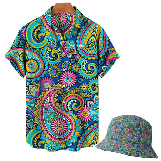 The Psychedelic Explorer Shirt is a short-sleeve button-up with a vibrant multicolored paisley and floral pattern in blue, pink, yellow, and green. Shown on a wooden hanger alongside a matching bucket hat.