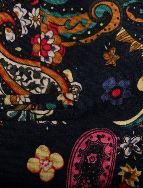 Close-up of the Navy Floral Blazers dark fabric, featuring a bold paisley and floral pattern in yellow, red, blue, orange, and pink. The vibrant textile shows a visible seam and folded corner for added detail.