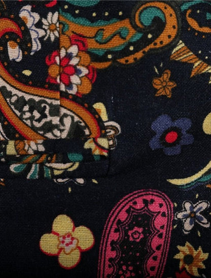 Close-up of the Navy Floral Blazers dark fabric, featuring a bold paisley and floral pattern in yellow, red, blue, orange, and pink. The vibrant textile shows a visible seam and folded corner for added detail.